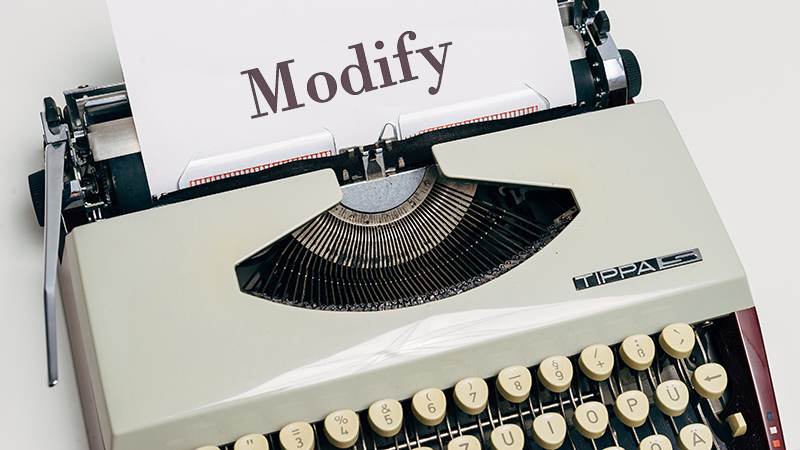 Typewriter and a white sheet containing the word "Modify".